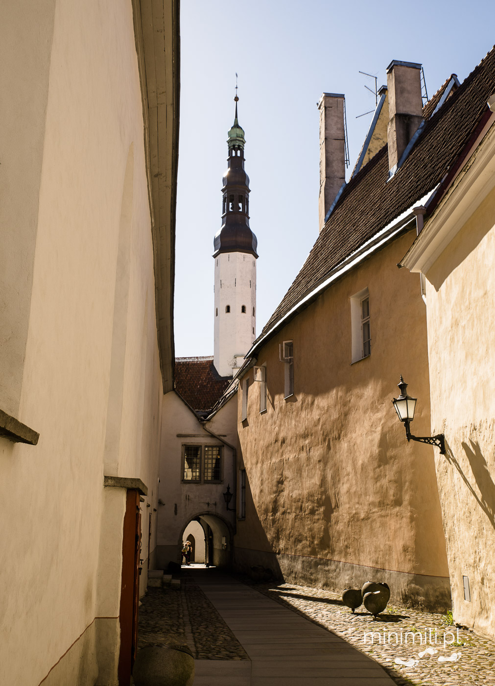 Wąska uliczka w Tallinnie z widokiem na wieżę ratusza.