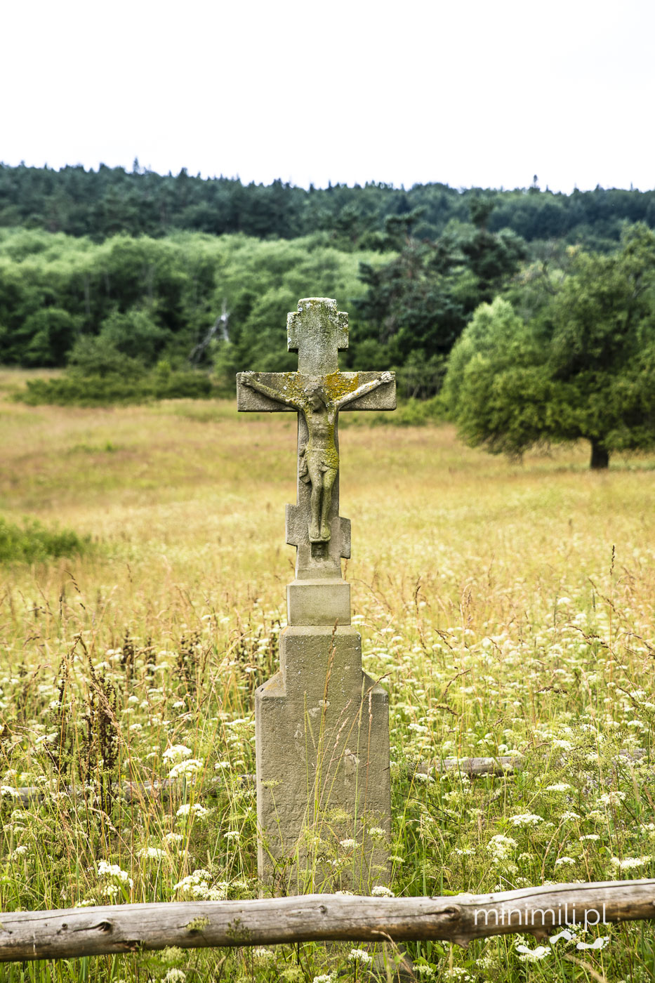 Przydrożny krzyż kamienny z figurą Jezusa wśród pól i wzgórz Beskidu Niskiego