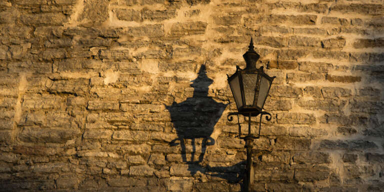 Zabytkowa latarnia rzucająca cień na kamienny mur w Tallinnie.